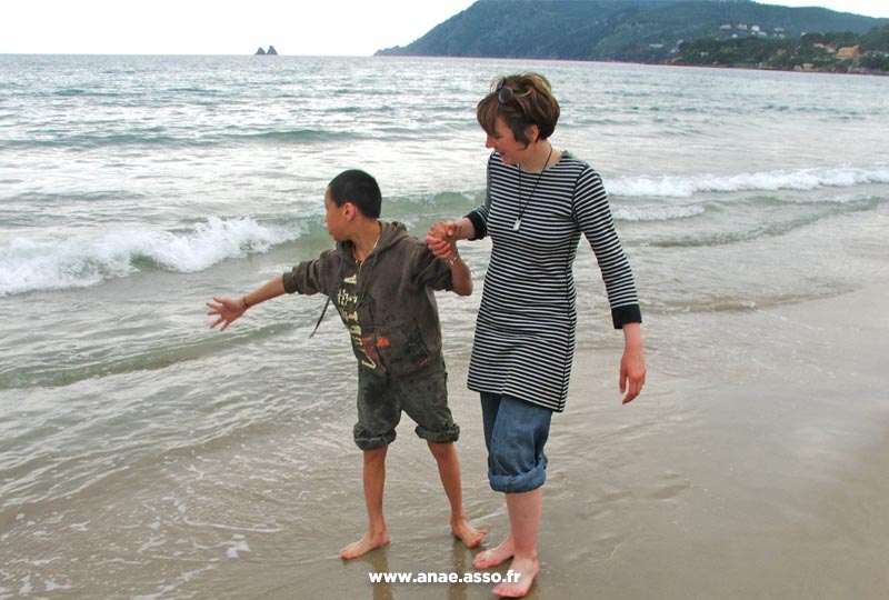 Une maman promène son fils en situation de handicap mental à la mer, en le tenant par la main
