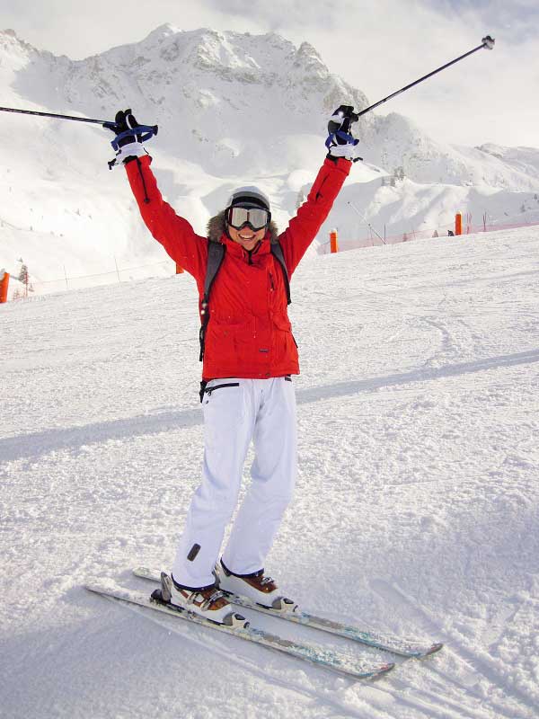 Une femme en train de skier lève les bras. Elle est heureuse de passer des vacances à la montagne.