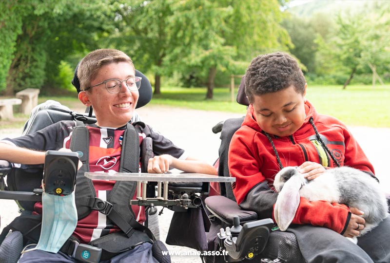 Séjour adapté jeune handicap moteur à Jambville près de Paris. Visite de la ferme pédagogique à Mantes la Ville. Deux enfants en fauteuil roulant électrique avec un lapin.