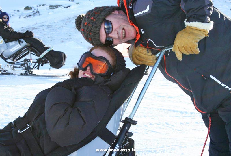 Séjour répit famille. Une jeune femme en vacances fait du ski assis adapté PMR avec un encadrant de l'association Anaé.