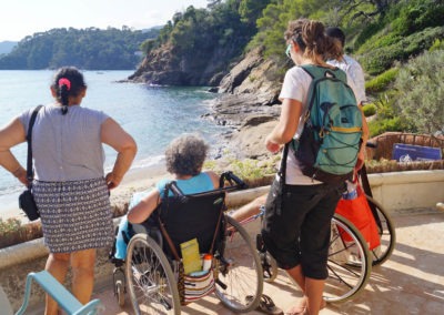 Séjour répit famille à la mer avec Anaé Vacances. Une dame en fauteuil roulant face à la mer avec ses accompagnateurs.