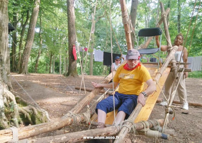 Séjour adapté PMR Anaé Vacances à Jambville l'été 2022. Un vacancier à mobilité réduite fait de la balançoire dans les bois avec son animatrice.