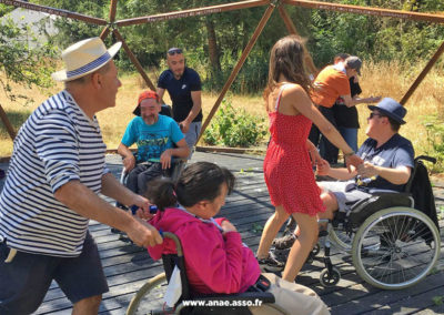 Séjour adapté PMR handicap Anaé Vacances à Jambville l'été 2022. Des vacanciers en fauteuil roulant et leurs animateurs en train de danser dehors sur du rock.