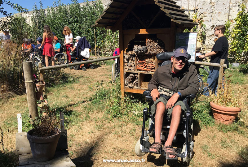 Séjour adapté PMR handicap Anaé Vacances à Jambville l'été 2022. Un vacancier en fauteuil roulant devant une ruche dans le potager du Château de Jambville.