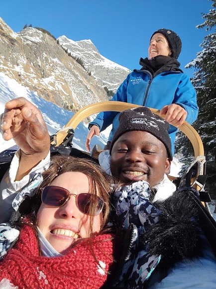 sejour-adapte-hiver-2022-montagne-pralognan-anae-vacances-chiens-traineaux Séjour adapté handicap hiver 2022. Une vacancière heureuse avec son accompagnateur en train de faire du chien de traîneaux.