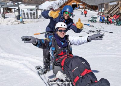 Un vacancier heureux et son moniteur de ski assis lors d'un séjour adapté PMR à la montagne en Savoie avec l'association Anaé