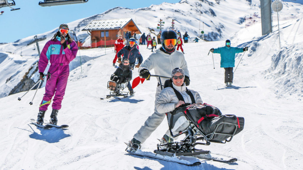Séjour adapté handicap hiver 2023 avec Anaé Vacances. Une femme à mobilité réduite est heureuse de faire du ski assis avec un moniteur.