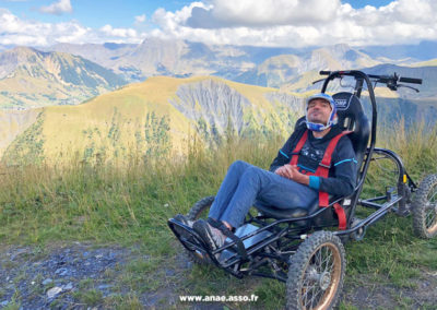 Activité adaptée PMR à la montagne. Un vacancier à mobilité réduite prend la pose dans un fauteuil tout terrain appelé Cimgo