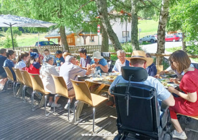 Séjour à la montagne. Un groupe de vacanciers prend son repas sur une grande table en terrasse au soleil.