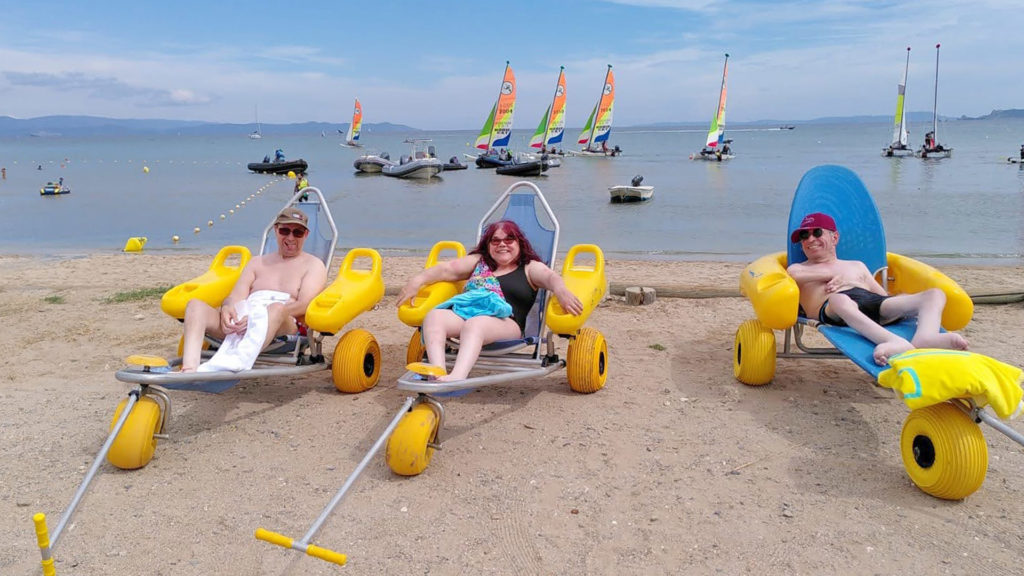3 vacanciers en situation de handicap moteur sur la plage de Hyères les Palmiers. Ils sont installés dans des Tiralo pour aller se baigner.