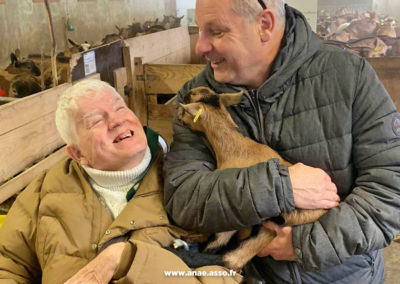 Séjour répit pour aidant et aidé avec Anaé vacances. Une personne en situation de handicap moteur visite la chèvrerie de Chavières à pralognan la Vanoise. Son accompagnateur lui montre un cabri et il rigole.