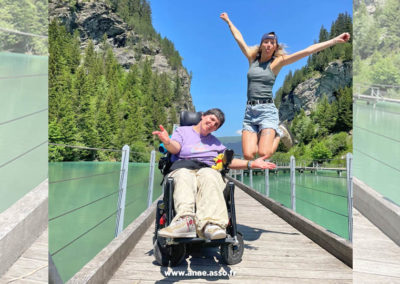 Séjour de vacances adaptées pour personnes en situation de handicap moteur. Une femme en fauteuil roulant prend un selfie avec son accompagnatrice.