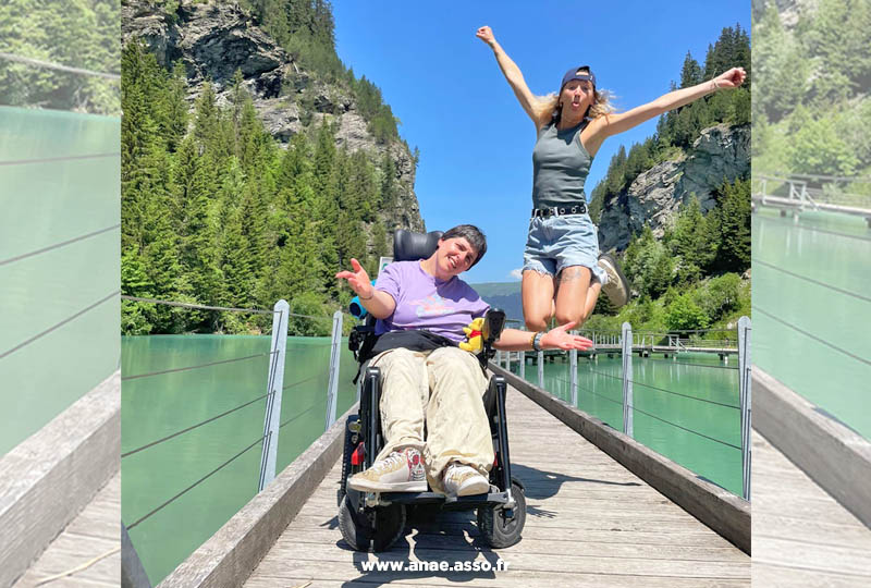 Séjour de vacances adaptées pour personnes en situation de handicap moteur. Une femme en fauteuil roulant prend un selfie avec son accompagnatrice.
