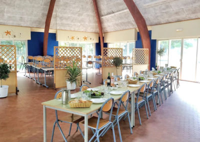 La salle à manger du centre de vacances Anaé La Rose des Vents à Piriac en Loire Atlantique. Il y a plusieurs grandes tables avec les couverts posés dessus.