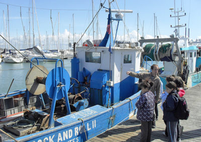 Un enseignant et ses élèves devant un bateau sur le port de Piriac lors d'une classe découverte à la mer. Ils font un séjour scolaire au centre de vacances Anaé La Rose des Vents à Piriac en Loire Atlantique.