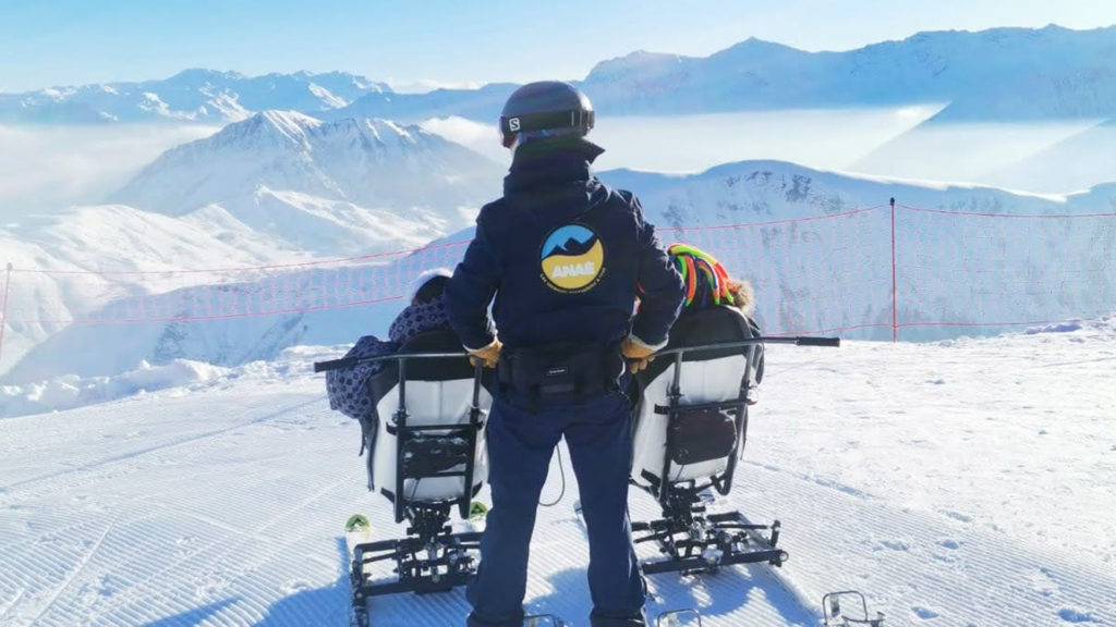 Un pilote de ski fauteuil et deux vacanciers qui font handiski. Activité adaptée PMR lors d'un séjour répit à la montagne avec Anaé Vacances à St-Sorlin d'Arves en Savoie.